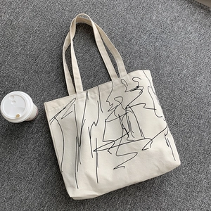 Overhead view of a minimalist cream canvas tote bag with abstract black line art pattern
