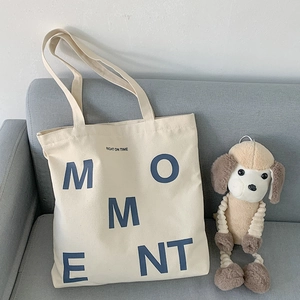Detail of a beige canvas tote bag with MOMENT print and a plush toy on a sofa