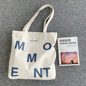 Detailed view of cream canvas tote bag with blue MOMENT print on textured grey rug