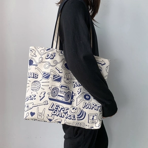 Detail of canvas tote bag featuring blue street graffiti print shown on a model's shoulder