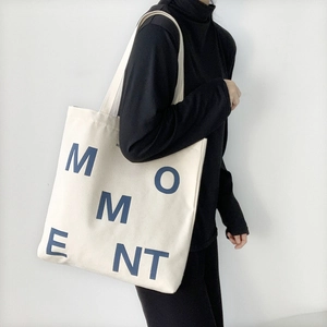 Detail of minimalist canvas tote bag with MOMENT print shown on a shoulder