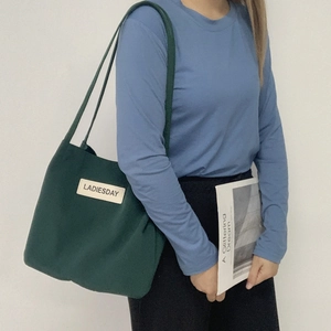 Detail of dark green nylon tote bag with white LADIESDAY label carried by a model