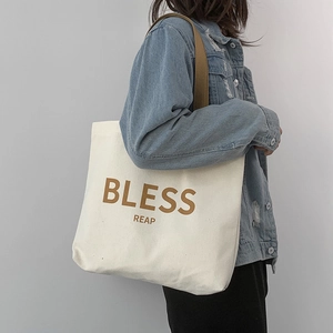 Vista laterale dettagliata della borsa tote in tela bianca con stampa marrone BLESS