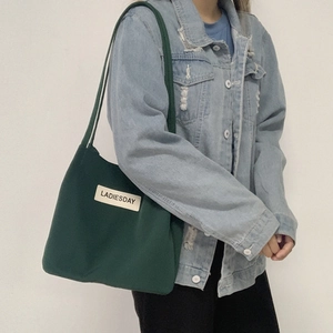 Deep green water-resistant nylon tote bag worn on shoulder over denim jacket
