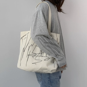 Detail of a large off-white canvas tote bag with black abstract art and wide straps