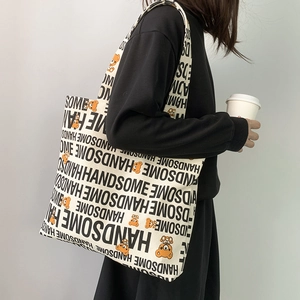 Detail of off-white canvas tote bag featuring repetitive letters and cartoon bear design