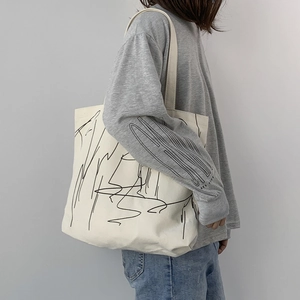 Detail of off-white canvas tote bag featuring minimalist abstract black line art on the side