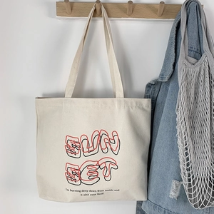 Close-up of cream canvas tote bag with SunSet graphic print hanging on a wooden hook