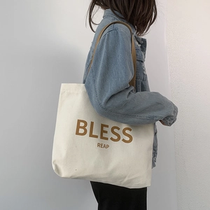 Dettaglio della borsa tote in tela bianca con scritte BLESS REAP marroni e tracolle
