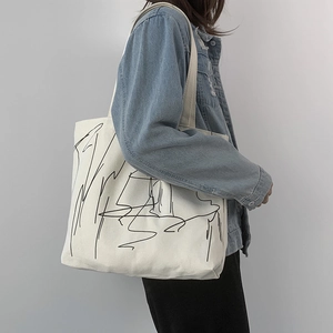 Large white canvas tote bag with abstract black lines shown on a shoulder model