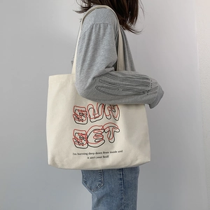 Detail of off-white canvas tote bag featuring SUN SET lettering and artistic quotes