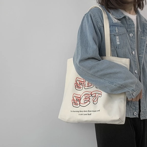 Detail of a beige canvas tote bag with SUNSET artistic lettering and thick handles