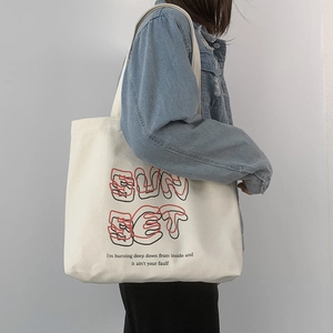 Detailed view of cream canvas tote bag featuring SUN SET print worn with denim jacket