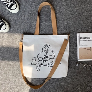 Detail of white canvas tote bag with black line art girl and dog illustration and brown strap