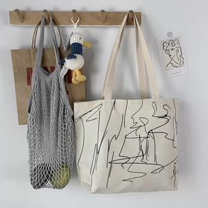 Artistic canvas tote with line art next to a mesh fruit bag on a wooden wall hook