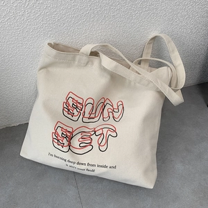 Detailed view of off-white canvas tote bag with red and black SUNSET letter printing