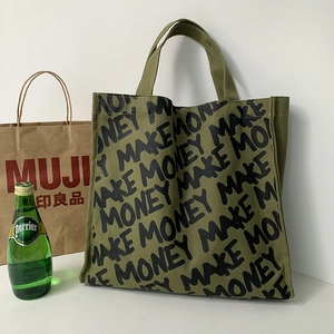 Detail of green canvas tote bag with MAKE MONEY print near a MUJI paper bag