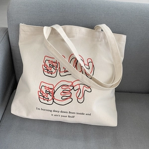 Detail of cream canvas tote bag with artistic typography on a grey fabric sofa