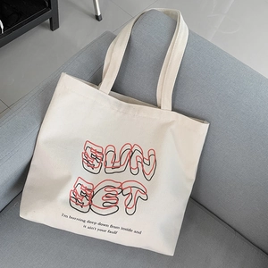 Detailed macro of a cream canvas tote bag with SunSet print on a soft grey sofa