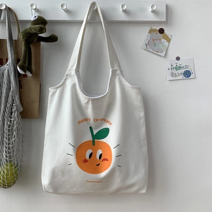 Dettaglio della tracolla larga e della stampa di arance sulla borsa tote in tela bianca