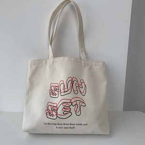 Detail of off-white canvas tote bag featuring SUNSET print and artistic typography