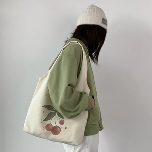 Detail of canvas tote bag with cherry illustration on green hoodie outfit