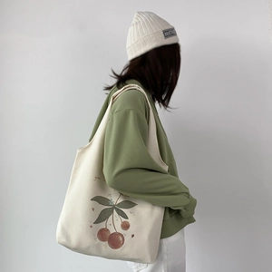 Detail of a beige canvas tote bag with a green cherry print and soft artistic lettering