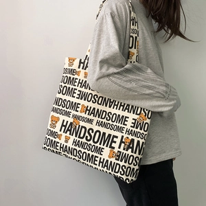 Detail view of cream canvas tote bag featuring bear print and repetitive letter pattern