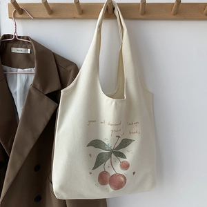 Detail of a minimalist canvas tote bag featuring a red cherry art print on a wooden hook