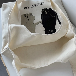 Close-up of cream canvas tote bag featuring a cute stuck-up cat illustration and text