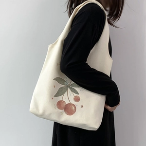 Detailed view of cream canvas tote bag with cherry print and green text on model