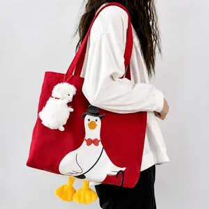Red canvas tote bag with cartoon duck print and white plush charm on a female model