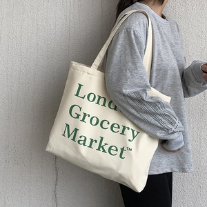 Detail of off-white canvas tote bag with London Grocery Market green text on shoulder