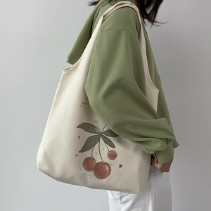 Canvas tote bag with cherry illustration and green text worn over shoulder by model