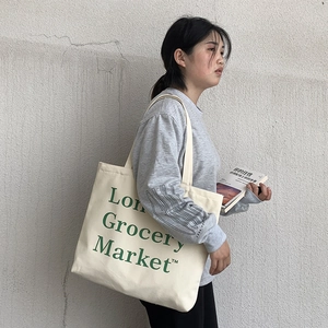 Detail of off-white canvas tote bag with green lettering shown on a model's shoulder
