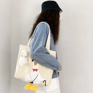 Detail of off-white canvas tote bag featuring a cute cartoon goose and plush charm