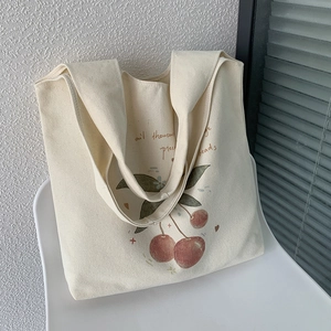Detailed shot of cream canvas tote bag featuring a realistic red cherry print design