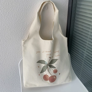 Detail of a beige canvas tote bag featuring a red cherry print and artistic script