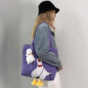 Detail of purple canvas tote bag with cartoon goose print and plush alpaca charm