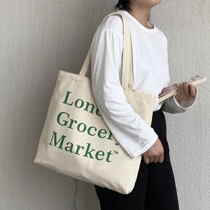 Detail of a beige canvas tote bag with green London Grocery Market print and cotton straps