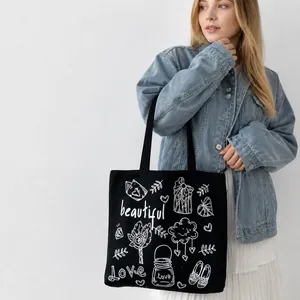 Borsa tote in tela nera con scarabocchi artistici bianchi indossata a spalla da modella