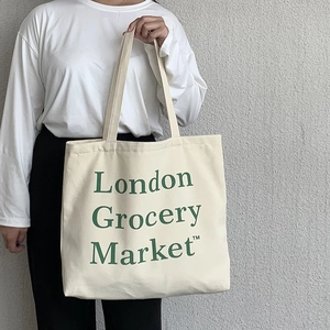 Detail of a large off-white canvas tote bag featuring green London Grocery Market text