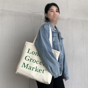 Street style shot of a cream canvas tote bag with green London Grocery Market print