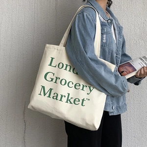 Detail of the London Grocery Market text on an off-white canvas tote bag worn on shoulder