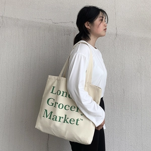 Minimalist beige canvas tote bag with green London Grocery Market print on shoulder