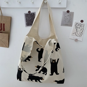 Close-up of cream canvas tote bag with black bear prints hanging on white wall hook