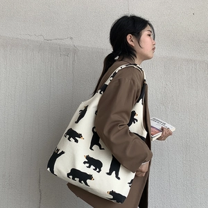 Close-up of off-white canvas tote bag featuring cute black cartoon bear patterns on shoulder