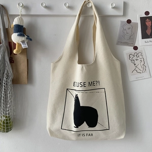 Detail of beige canvas tote bag featuring alpaca illustration and slogan on white hook