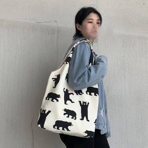 Detail of a large canvas tote bag with black cartoon bear patterns on model's shoulder