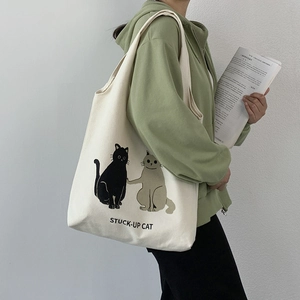Detail of off-white canvas tote bag featuring cute cartoon cat print and shoulder strap